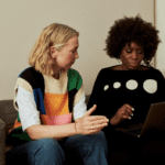 Two women sitting on a couch looking at a screen