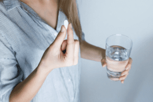 A woman holding a pill in one hand and a half-filled glass of water in the other