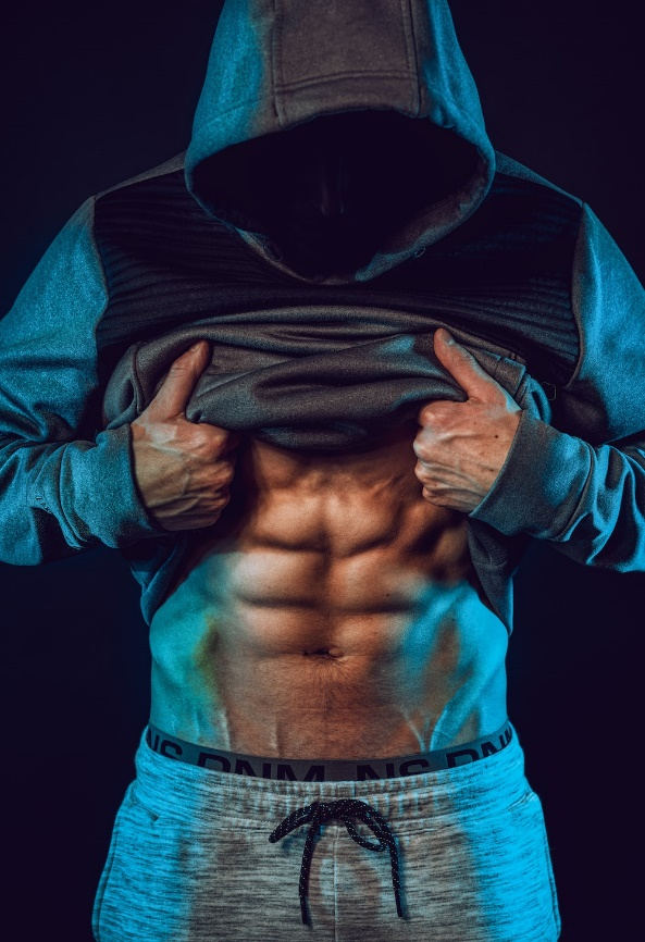  Muscular athlete lifting his hoodie to reveal a well-defined abdomen, symbolizing bodybuilding achievement.