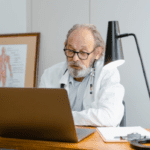 A doctor is using a laptop in his office.