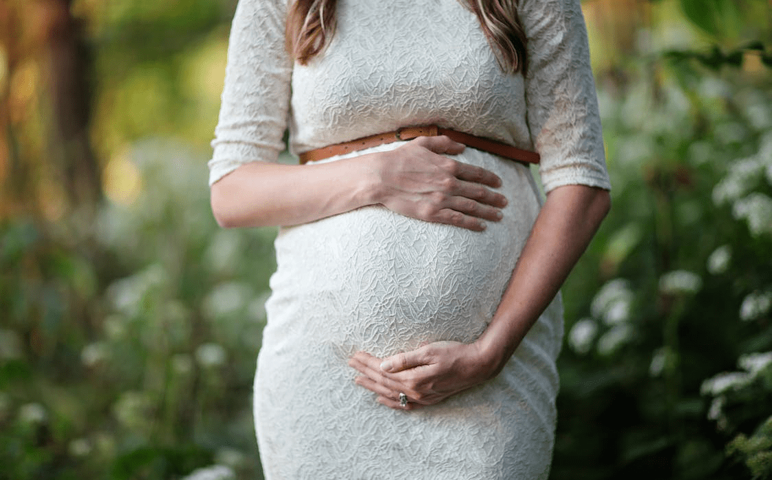 A woman is holding her baby bump while posing for a photograph