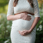 A woman is holding her baby bump while posing for a photograph